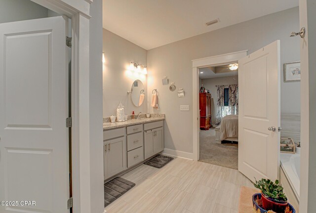 ensuite bathroom with connected bathroom, a washtub, visible vents, vanity, and baseboards