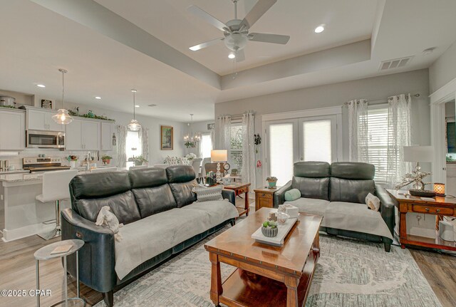 living room with ceiling fan, recessed lighting, visible vents, light wood-type flooring, and a tray ceiling