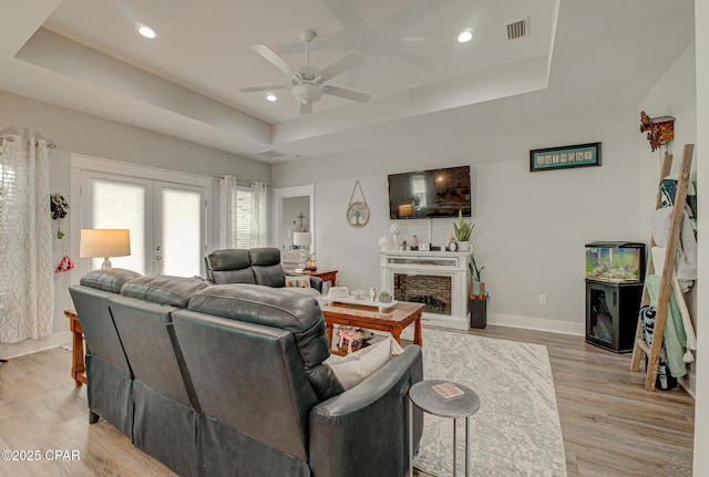 living room featuring a fireplace with raised hearth, a tray ceiling, light wood-style flooring, and visible vents