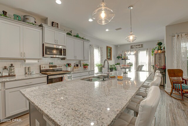 kitchen with a sink, a kitchen breakfast bar, appliances with stainless steel finishes, backsplash, and a center island with sink