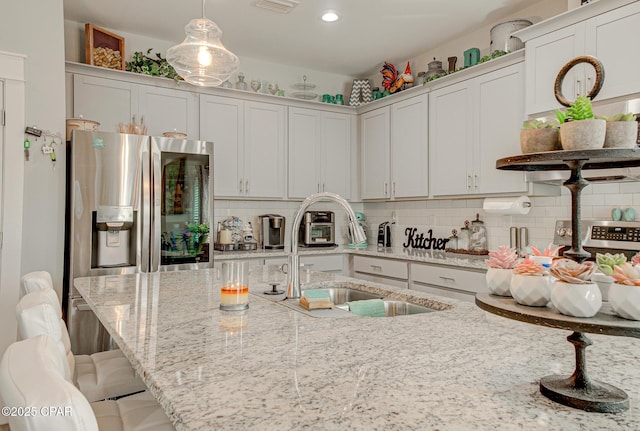 kitchen featuring decorative backsplash, a kitchen breakfast bar, decorative light fixtures, stainless steel refrigerator with ice dispenser, and a sink