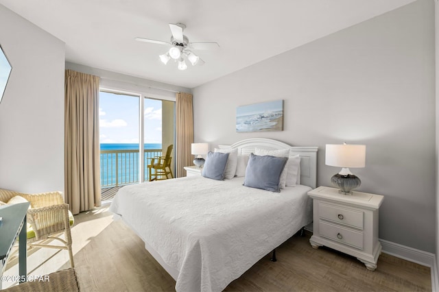 bedroom featuring wood finished floors, a water view, access to exterior, baseboards, and a ceiling fan