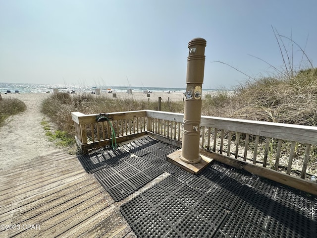 wooden terrace featuring a beach view and a water view