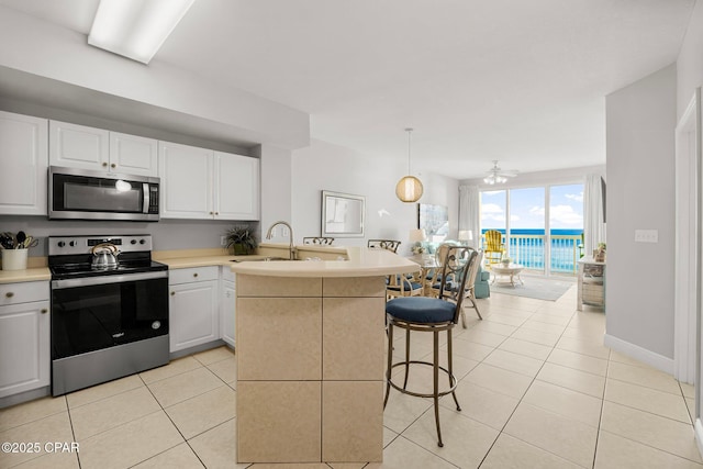 kitchen featuring a sink, light tile patterned flooring, a breakfast bar, a peninsula, and appliances with stainless steel finishes