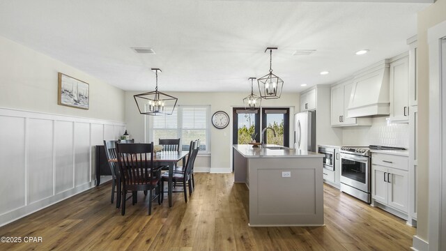 kitchen with premium range hood, a sink, visible vents, appliances with stainless steel finishes, and a center island with sink