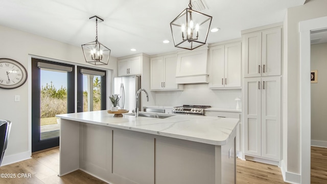 kitchen featuring light wood finished floors, custom exhaust hood, appliances with stainless steel finishes, a sink, and a chandelier