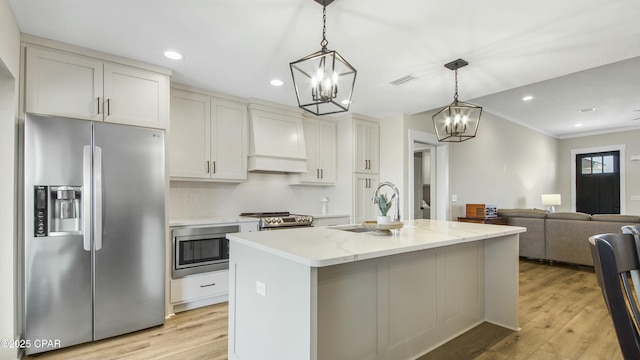 kitchen featuring stainless steel appliances, hanging light fixtures, light wood-style flooring, and an island with sink