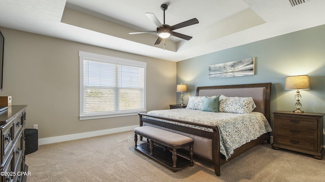 bedroom with light colored carpet, visible vents, a ceiling fan, baseboards, and a tray ceiling