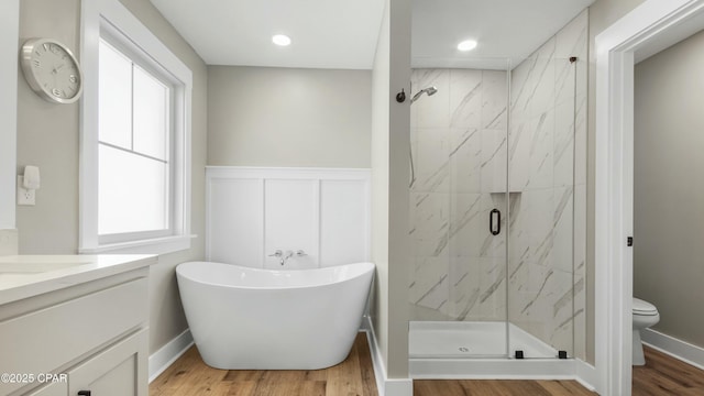 full bathroom featuring a marble finish shower, wainscoting, toilet, a soaking tub, and wood finished floors