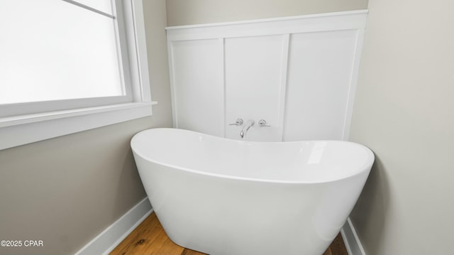 full bathroom with a freestanding tub, baseboards, and wood finished floors