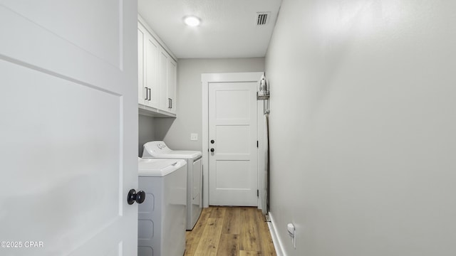 clothes washing area featuring cabinet space, visible vents, light wood-style floors, and washing machine and clothes dryer