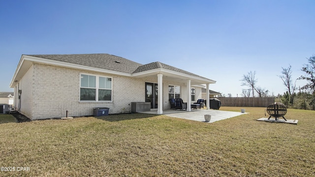 rear view of property with brick siding, fence, roof with shingles, a lawn, and a patio area