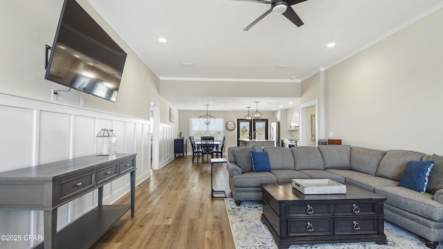 living room featuring ceiling fan with notable chandelier, ornamental molding, light wood-style flooring, and a decorative wall