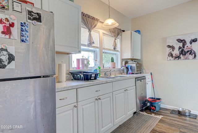 kitchen featuring stainless steel appliances, wood finished floors, a sink, white cabinetry, and light countertops