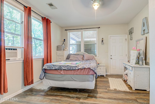 bedroom with ceiling fan, cooling unit, wood finished floors, visible vents, and baseboards