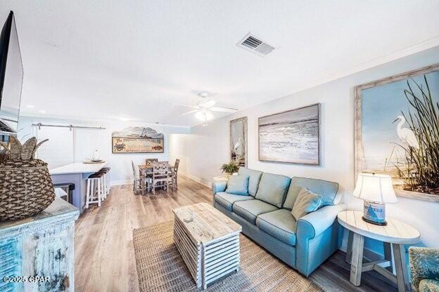 living area with ceiling fan, wood finished floors, visible vents, and baseboards