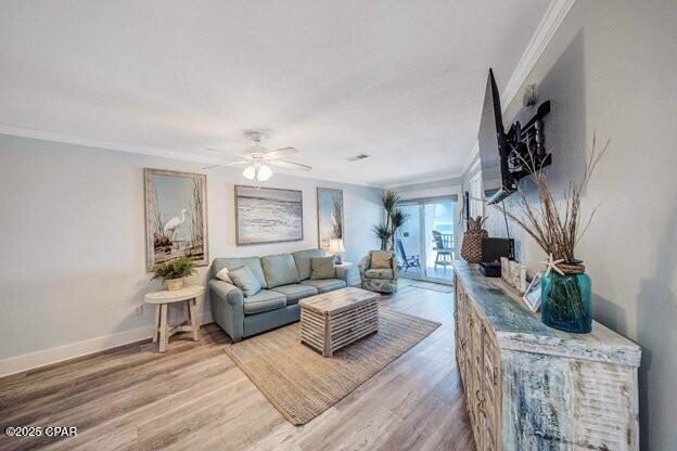 living area featuring baseboards, wood finished floors, a ceiling fan, and crown molding