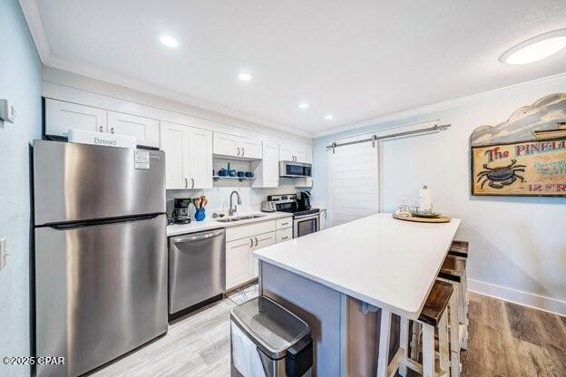 kitchen with a barn door, appliances with stainless steel finishes, a kitchen breakfast bar, white cabinetry, and a sink