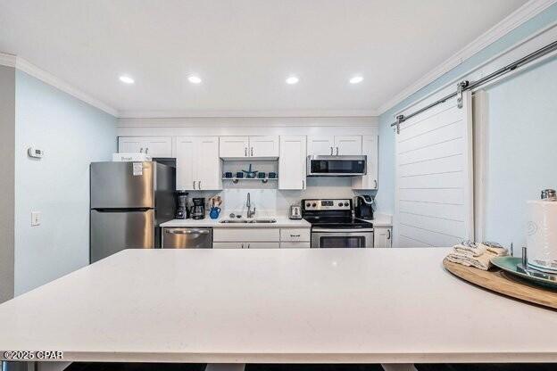 kitchen featuring a barn door, appliances with stainless steel finishes, ornamental molding, white cabinetry, and a sink