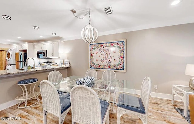 dining room with stacked washer and dryer, light wood finished floors, baseboards, visible vents, and a notable chandelier