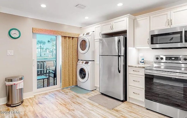 kitchen with visible vents, stainless steel appliances, stacked washer and dryer, and light wood-style flooring