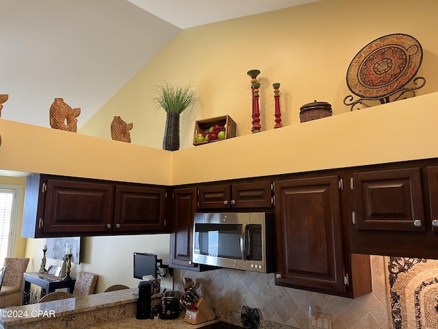 kitchen with dark brown cabinetry, tasteful backsplash, stainless steel microwave, and vaulted ceiling