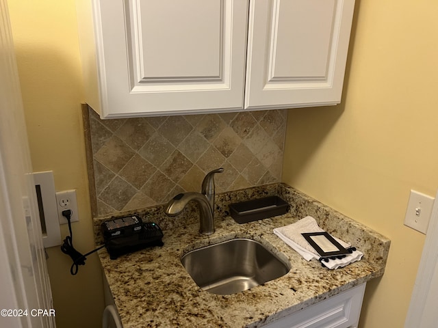 kitchen with white cabinetry, a sink, decorative backsplash, and light stone countertops