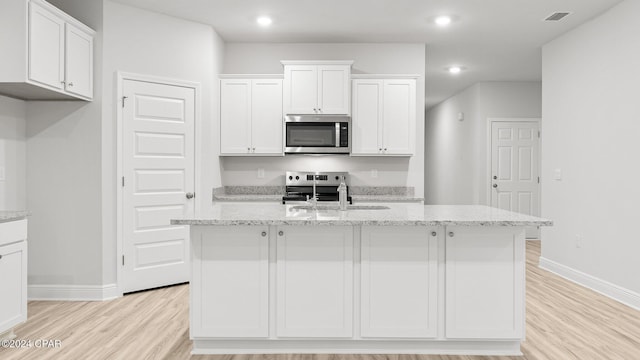 kitchen featuring stainless steel microwave, a center island with sink, white cabinetry, and light wood-style floors