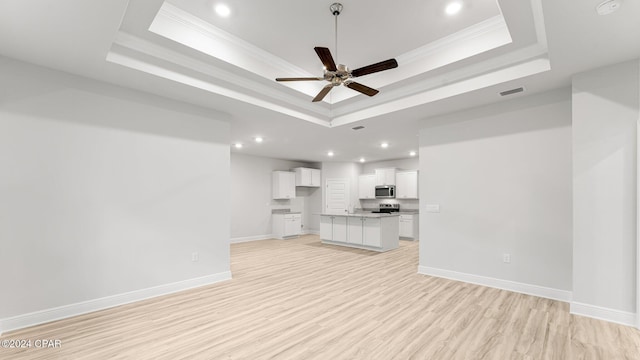 unfurnished living room with light wood-style flooring, visible vents, baseboards, a tray ceiling, and crown molding