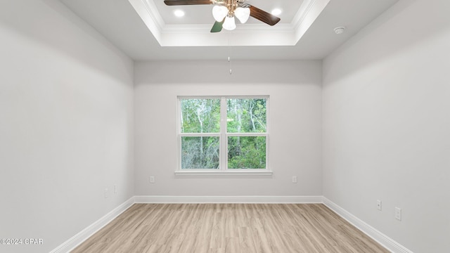 empty room with baseboards, a tray ceiling, wood finished floors, and ornamental molding