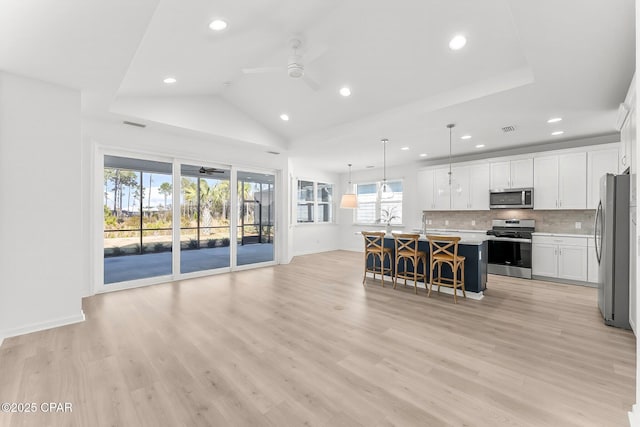 kitchen featuring ceiling fan, open floor plan, a breakfast bar, decorative backsplash, and appliances with stainless steel finishes