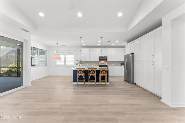 kitchen with backsplash, light countertops, appliances with stainless steel finishes, a kitchen breakfast bar, and white cabinets