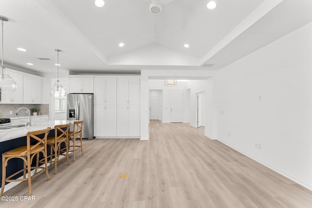 kitchen with lofted ceiling, stainless steel fridge with ice dispenser, a sink, decorative backsplash, and white cabinets