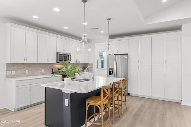 kitchen featuring appliances with stainless steel finishes, white cabinetry, light wood-style floors, and a sink