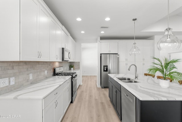 kitchen featuring visible vents, stainless steel appliances, a large island, white cabinetry, and a sink