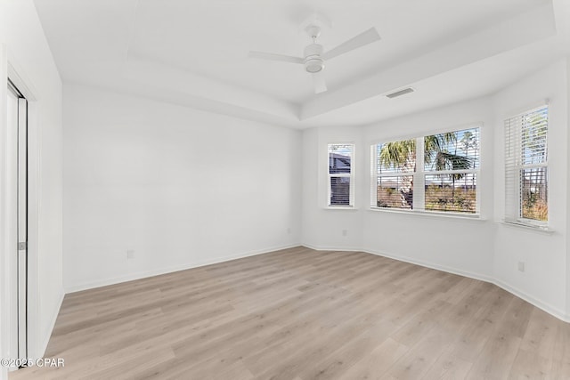 spare room with light wood finished floors, visible vents, baseboards, and a tray ceiling