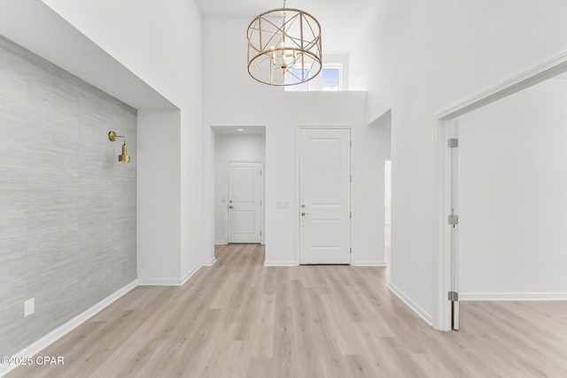 foyer entrance with a high ceiling, a notable chandelier, baseboards, and light wood finished floors