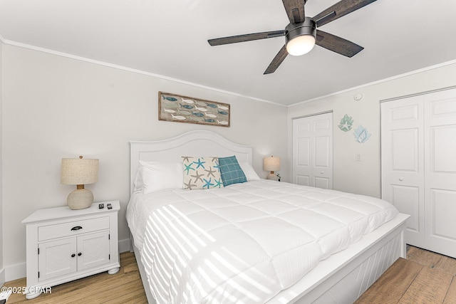 bedroom featuring baseboards, a ceiling fan, ornamental molding, light wood-type flooring, and multiple closets