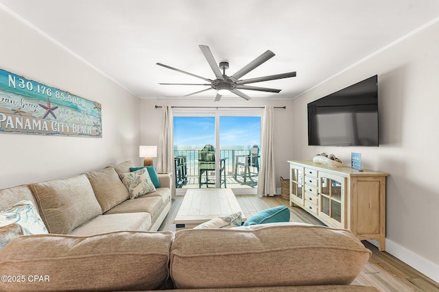 living area featuring light wood-style flooring, ornamental molding, ceiling fan, and baseboards