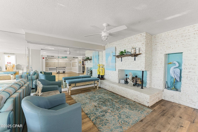 living room featuring a ceiling fan, a brick fireplace, a textured ceiling, and wood finished floors