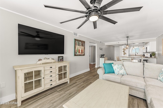 living area with ceiling fan, arched walkways, visible vents, baseboards, and light wood finished floors