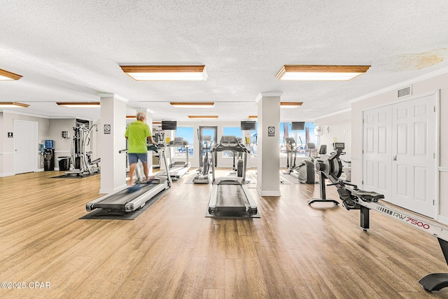 workout area featuring ornamental molding, visible vents, a textured ceiling, and wood finished floors