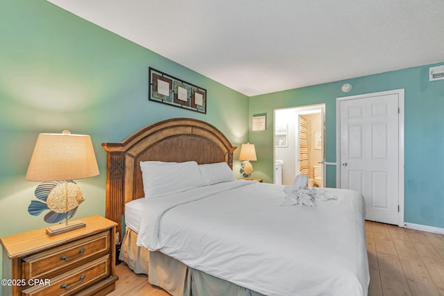 bedroom with light wood-style flooring, baseboards, and connected bathroom