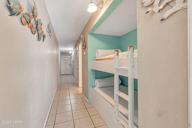 corridor featuring a textured wall, a textured ceiling, baseboards, and tile patterned floors