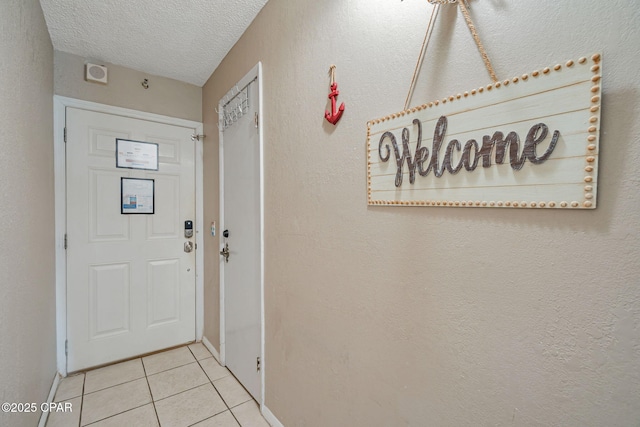 doorway with a textured wall, a textured ceiling, and tile patterned floors