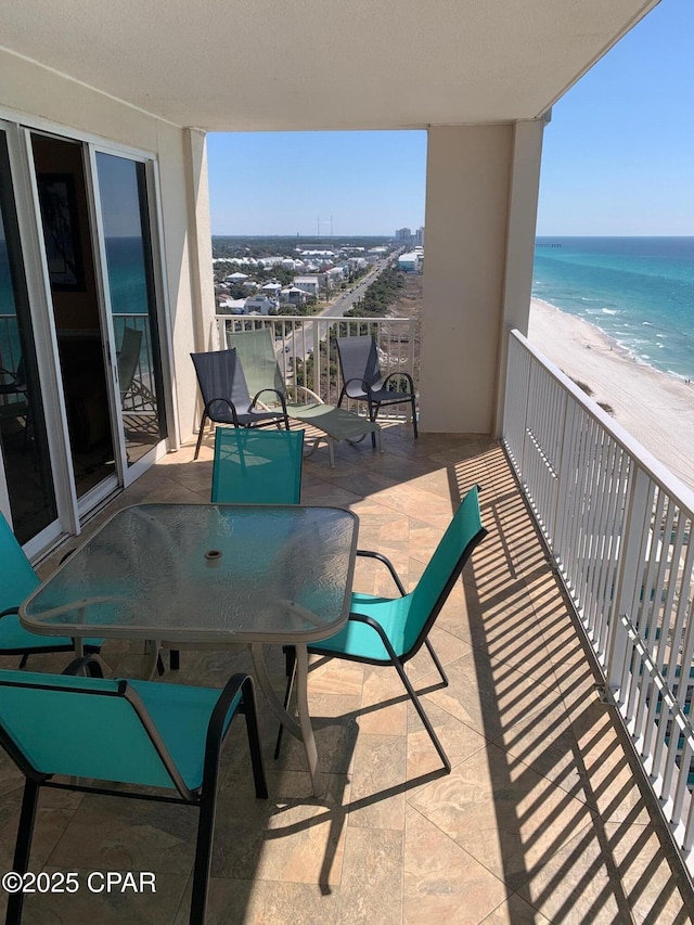 balcony with a water view, outdoor dining area, and a view of the beach