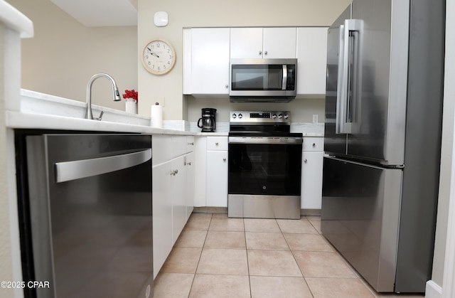 kitchen featuring light tile patterned floors, stainless steel appliances, light countertops, white cabinets, and a sink