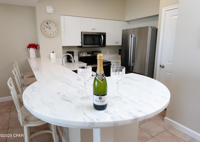 kitchen featuring stainless steel appliances, light tile patterned flooring, white cabinetry, a peninsula, and a kitchen bar