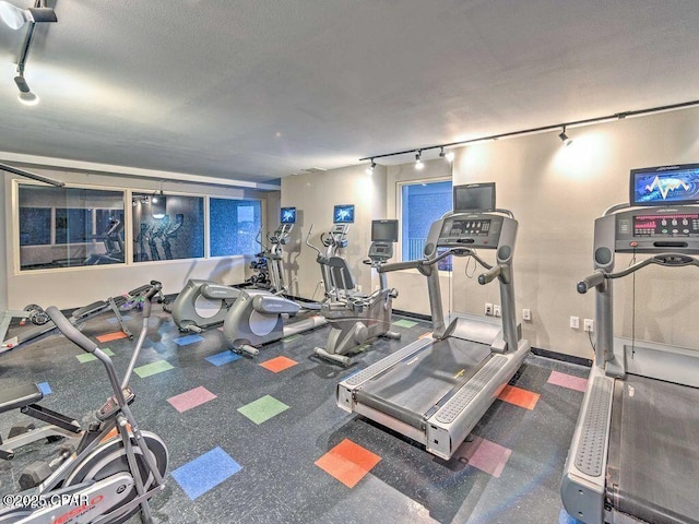 exercise room featuring a textured ceiling, rail lighting, and baseboards