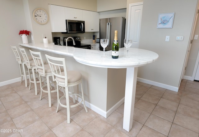 kitchen with a breakfast bar, light tile patterned floors, appliances with stainless steel finishes, a peninsula, and baseboards